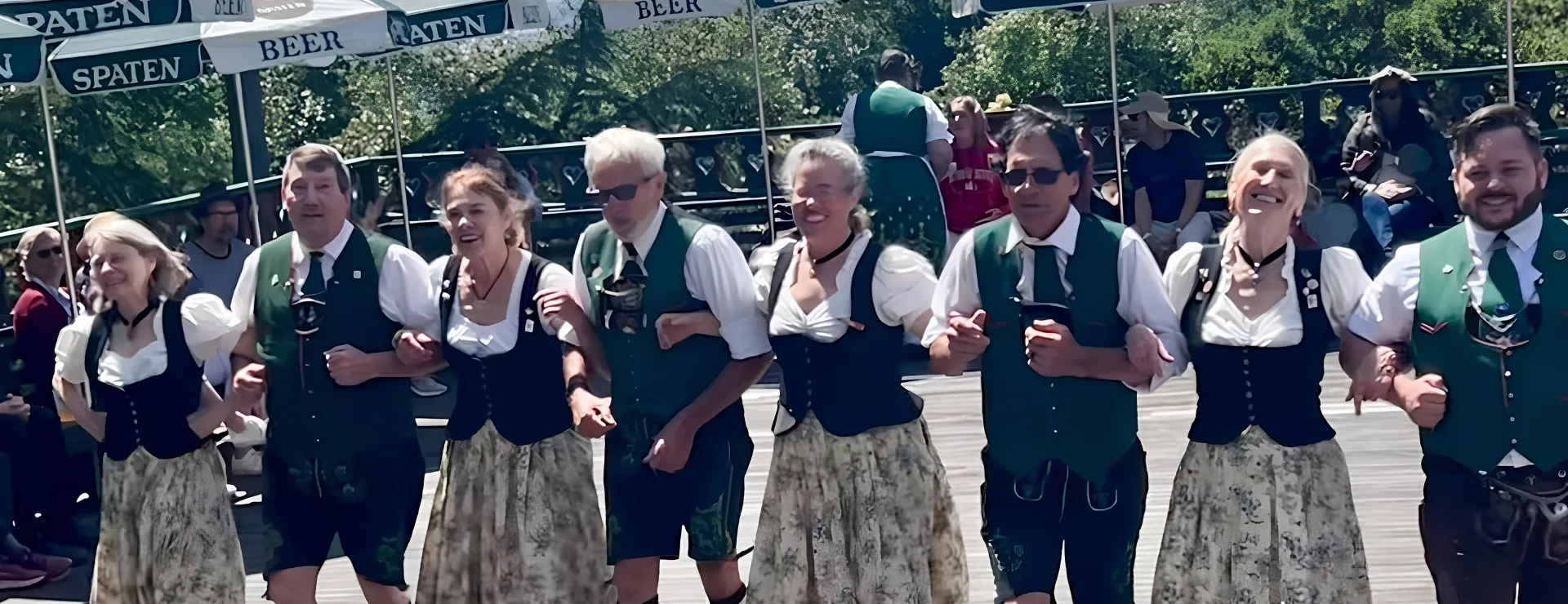Dancers in Dirndl and Lederhosen link arms at the Oakland Nature Friends Maifest, with a ribboned maypole